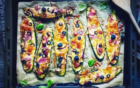 Zucchini-Hälften mit Käse, Oliven, Zwiebeln und Salami, die wie Pizza belegt sind. Sie schmeckt zucchini auf pizza!