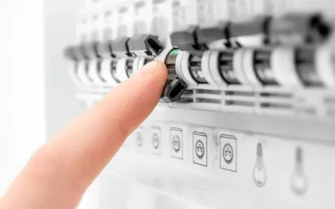 Doigt actionnant un disjoncteur dans un tableau électrique. Aide à comprendre quel disjoncteur différentiel choisir pour votre installation.