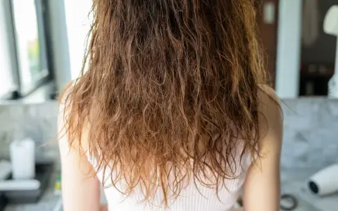 Wilgotne, brązowe włosy z widocznym **frizz** opadają na ramiona.