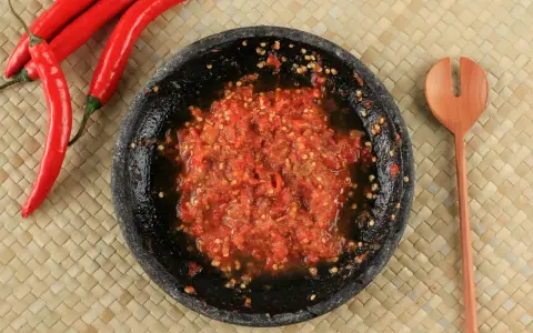 Świeżo przygotowany sos sambal w kamiennym moździerzu, obok czerwone papryczki chili i drewniana łyżka.