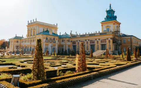 Barokowy pałac z żółtą fasadą i zielonym dachem, otoczony geometrycznym ogrodem. Wnętrze pałacu zachwyca bogactwem zdobień.