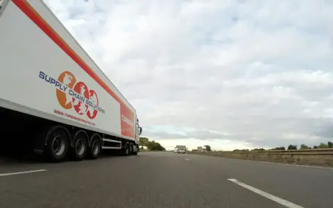 Camión de carga con el logo "Supply Chain Solutions" y "Turners" avanza por la autopista.