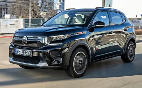 Czarny Citroen C3 porusza się po mieście, odbijając światła i budynki w swojej lśniącej karoserii.