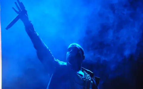 Kanye West z mikrofonem w dłoni, w niebieskiej poświacie. W tle dym, przypominający atmosferę z jego albumów.