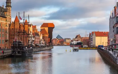 Gdańsk: zabytkowy żaglowiec cumuje przy Motławie, w tle Żuraw i nowoczesne budynki. Malowniczy opis miasta.