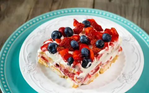Tranche de tiramisu aux fruits rouges, garnie de fraises et myrtilles fraîches. Un délice estival.