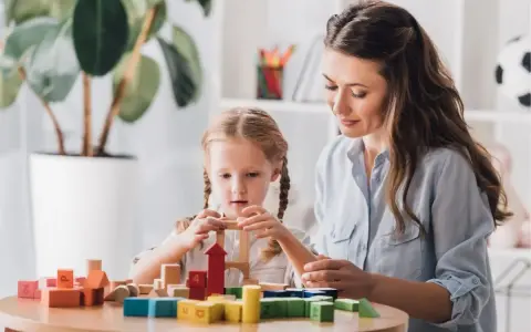 Kobieta i dziewczynka budują wieżę z kolorowych klocków.