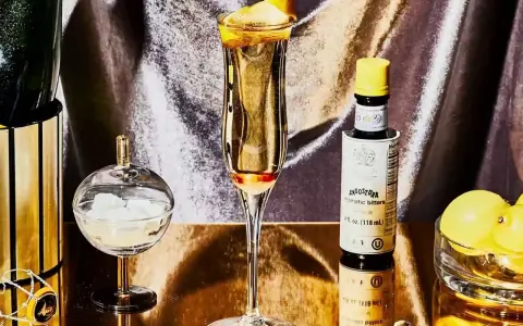 Elegantes Glas mit einem Champagner-Cocktail, garniert mit Zitronenschale. Daneben eine Flasche Angostura, Zuckerwürfel und Zitronen.