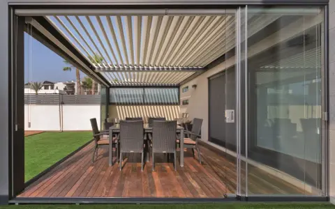 Porches cerrados con encanto, con mesa y sillas de mimbre sobre tarima de madera y césped artificial.