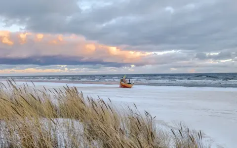Ein kleines Boot liegt am verschneiten Strand der Ostsee, im Hintergrund die Seebrücke von Ahlbeck.