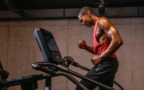 Schwitzender Mann im roten Tanktop läuft auf Laufband. Perfektes Cardio nach dem Krafttraining.