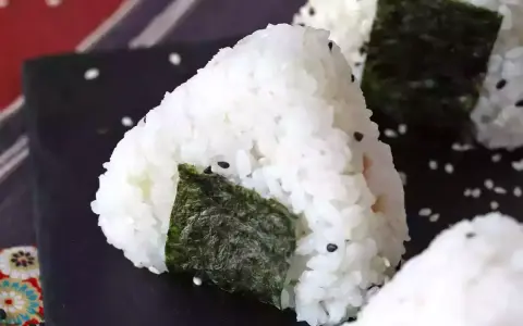 Trójkątne onigiri z tuńczykiem, ryżem i wodorostami nori, posypane sezamem.