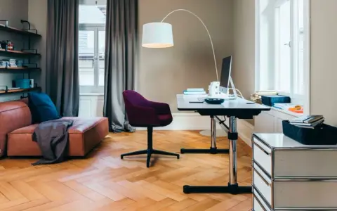 Accogliente stanza studio piccola con divano in pelle, scrivania regolabile, sedia viola e libreria a muro.
