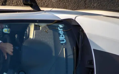 Fahrer hält das Lenkrad eines Autos mit Uber-Aufkleber auf der Windschutzscheibe.