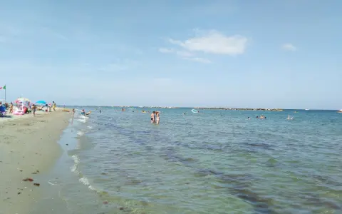 Gente che si gode il sole e il mare a Lido Adriano. Bambini giocano sulla sabbia, adulti nuotano e si rilassano nell'acqua cristallina.