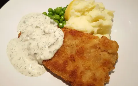 Panerad fisk med krämig kall sås till, serverad med potatismos, gröna ärtor och en citronklyfta.