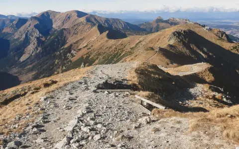 Kamienista ścieżka prowadzi przez trawiaste zbocza, ukazując najpiękniejsze doliny Zakopane. W oddali majaczą góry.