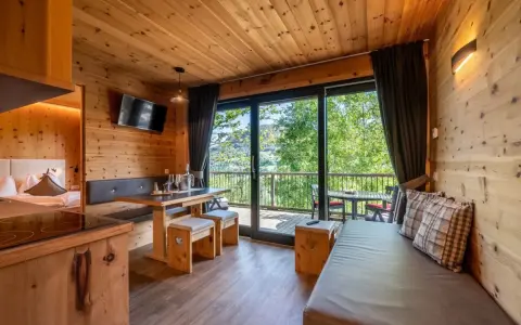Przytulny domek z widokiem na góry, idealny na camping Seiser Alm. Drewniane wnętrze, wygodna kanapa i stół zapraszają do relaksu.