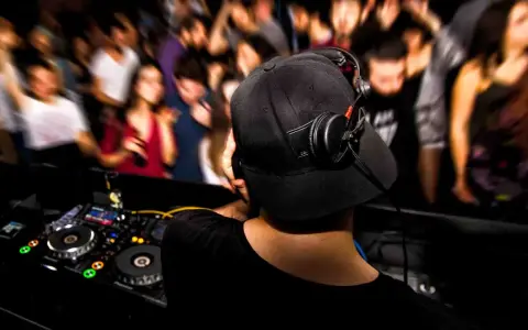 DJ aux platines, casque sur les oreilles, gérant le niveau sonore pour une foule en délire.