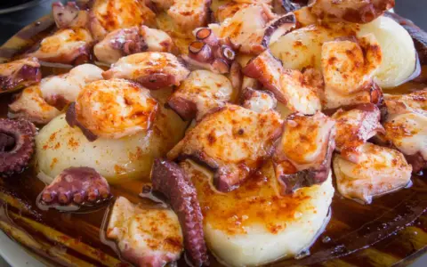 Pulpo a la gallega servido en plato de madera, con patatas cocidas y espolvoreado con pimentón.