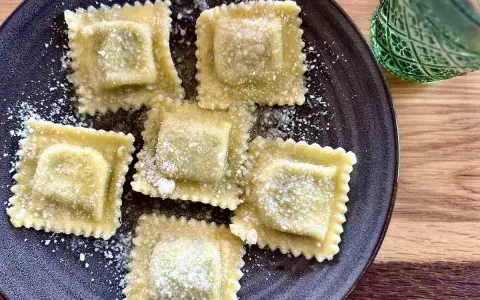 Pięć kwadratowych ravioli posypanych parmezanem na ciemnym talerzu. Idealne do domowego ravioli przepis.
