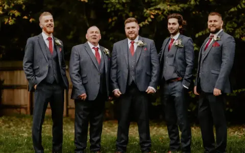 Five men in matching grey suits with red ties and pocket squares. The price of tuxedos can vary, but these look like a good investment for a wedding party.