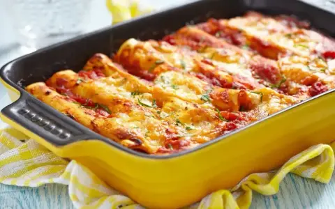 Pyszne cannelloni z mięsem mielonym, zapieczone pod sosem pomidorowym i serem, w żółtym naczyniu.
