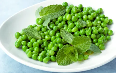 Petits pois frais et menthe sur une assiette blanche, une idée simple pour une recette de petit pois légère et savoureuse.