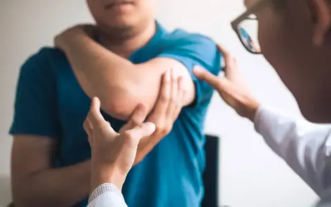 Un médecin examine le coude d'un patient, possiblement atteint du syndrome de la souris, une maladie professionnelle liée à l'usage intensif de l'ordinateur.