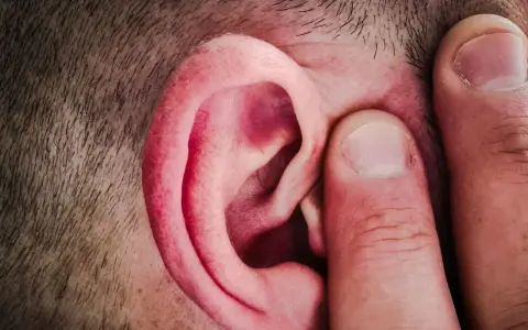 Un doigt pince l'oreille d'un homme, comme pour mieux capter un son aigu.