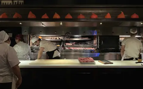 Chefs preparan cortes de carne en la parrilla Don Julio, con brasas ardientes y un ambiente de cocina profesional.