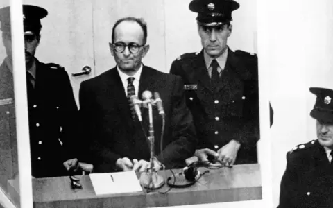 Adolf Eichmann w szklanej kabinie, otoczony strażnikami. Jego proces był transmitowany na cały świat, budząc grozę i pytania o losy dzieci.