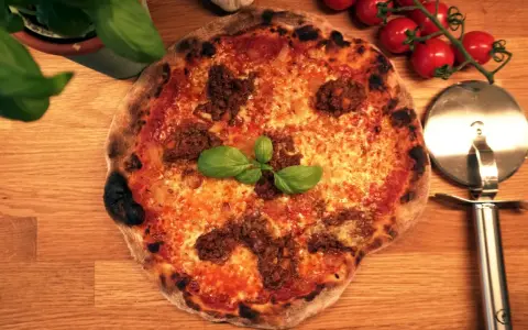 En napolitansk pizza med köttfärs som topping, garnerad med färsk basilika. Bredvid ligger en pizzaskärare och körsbärstomater.