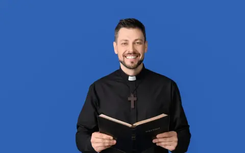 Uśmiechnięty ksiądz w czarnej sutannie z krzyżykiem trzyma otwartą Biblię. Idealny obrazek na podziękowania dla księdza.