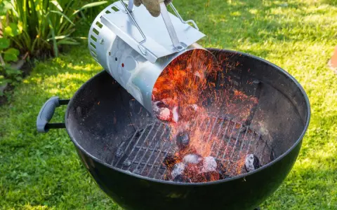 Encendiendo carbón con un chimenea para barbacoa. Chispas vuelan mientras se vierten las brasas calientes.