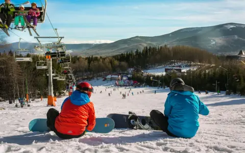 Dwaj snowboardziści odpoczywają na stoku, w tle widać wyciąg narciarski Karpacz i góry.