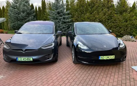 Dwa samochody Tesla, jeden ciemnoszary Model X, drugi czarny Model Y, stoją na podjeździe.