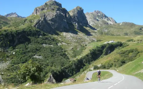 Ciclista su strada tortuosa verso il Cormet de Roselend, con montagne imponenti e verdi pendii.
