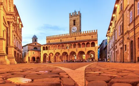 Piazza del Popolo a Ripatransone, un gioiello per un itinerario Marche 5 giorni. Edifici storici illuminati, torre con orologio e ciottoli antichi.