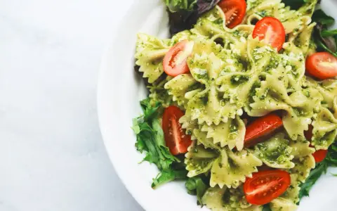 Pyszna sałatka z makaronem farfalle w sosie pesto, z pomidorkami koktajlowymi i świeżą sałatą.