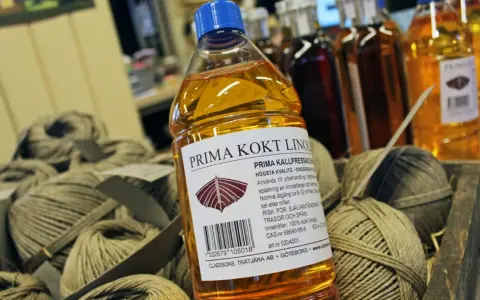 En flaska Prima kokt linolja, perfekt för fernissa oljemålning och ytbehandling av trä. Bredvid ligger härvor av garn.