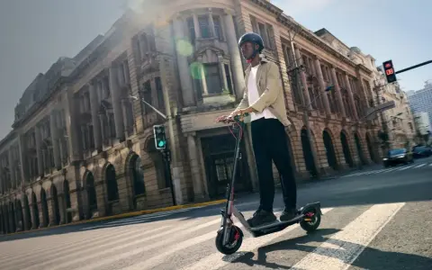 Un homme en casque roule sur la trottinette électrique la plus rapide du monde, traversant une rue bordée de bâtiments historiques.