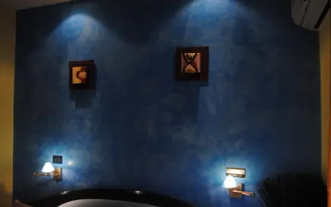 Pared azul con efecto veladura, dos cuadros abstractos y lámparas de pared.