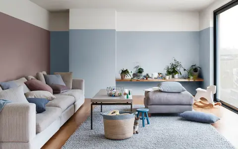 Soggiorno accogliente con divano beige, tappeto grigio e pareti color carta da zucchero. Un coniglietto curioso osserva dal cesto.