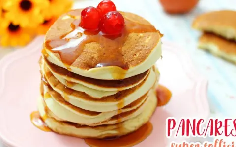 Pancakes senza glutine, soffici e dorati, impilati su un piatto rosa, con sciroppo d'acero e ciliegie rosse.