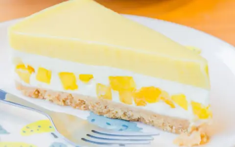 Pyszny sernik mango z kawałkami owoców i kremową warstwą na kruchym spodzie.
