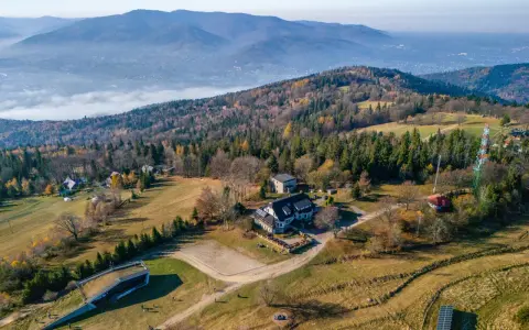 Widok z lotu ptaka na górski krajobraz jesienią. Widać budynki, lasy i dolinę z mgłą. Taki widok to prawdziwy przegibek!