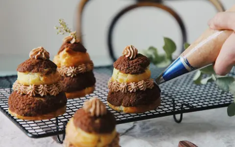 Finition d'une religieuse au chocolat avec une touche de crème. Ces pâtisseries sont prêtes à être dégustées.