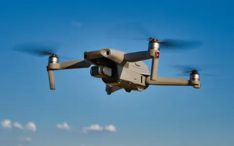 Grauer DJI Mavic Air 2 Drohne fliegt im blauen Himmel. Mit Drohnen Versicherung sind Sie sicher unterwegs.