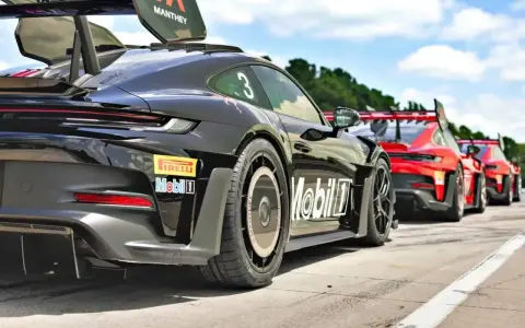 Czarny Porsche GT3 RS z numerem 3 i logo Manthey na skrzydle, gotowy do wyścigu obok czerwonych samochodów.